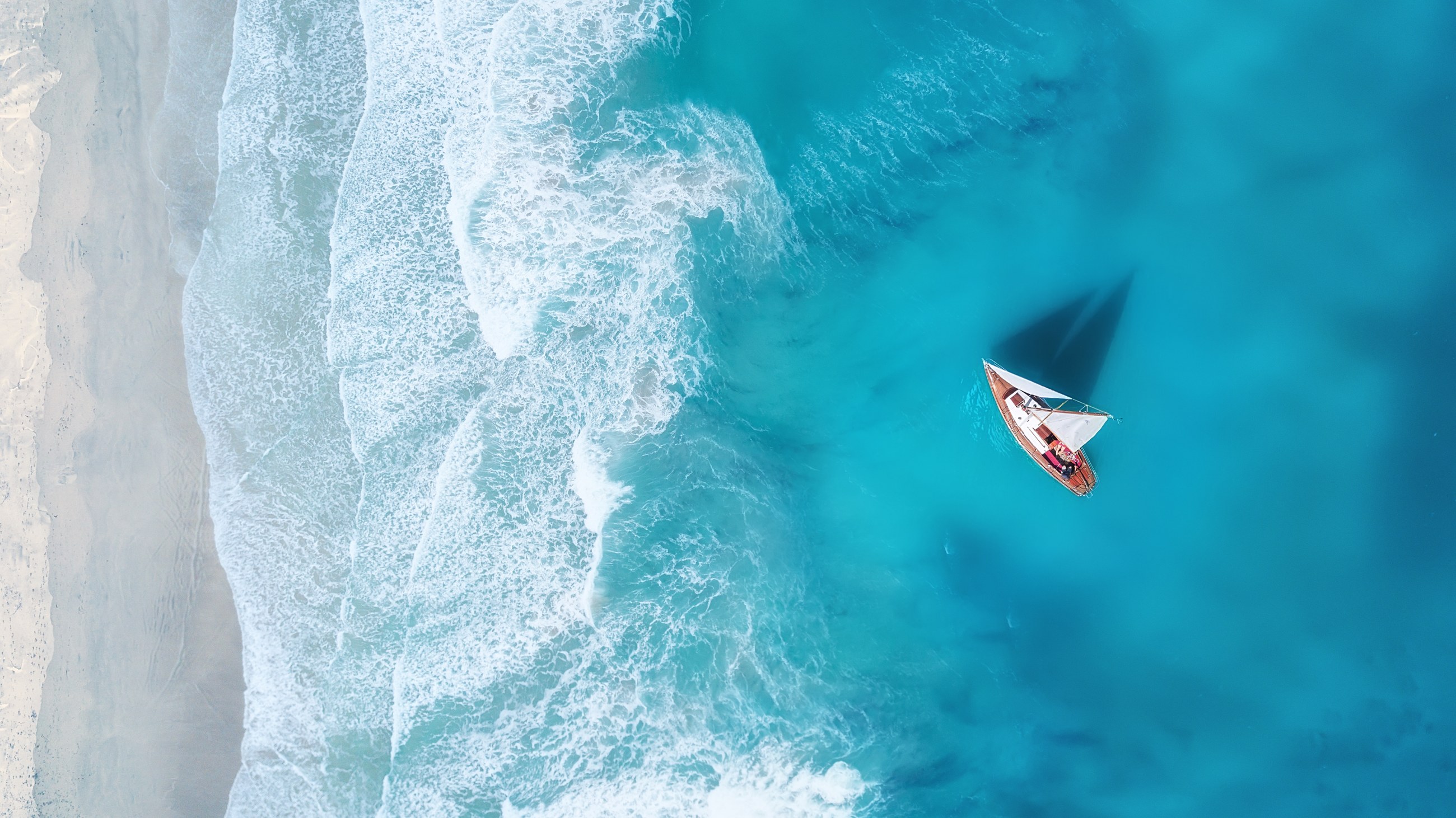 Aerial view of a sailboat over turquoise water and breaking waves